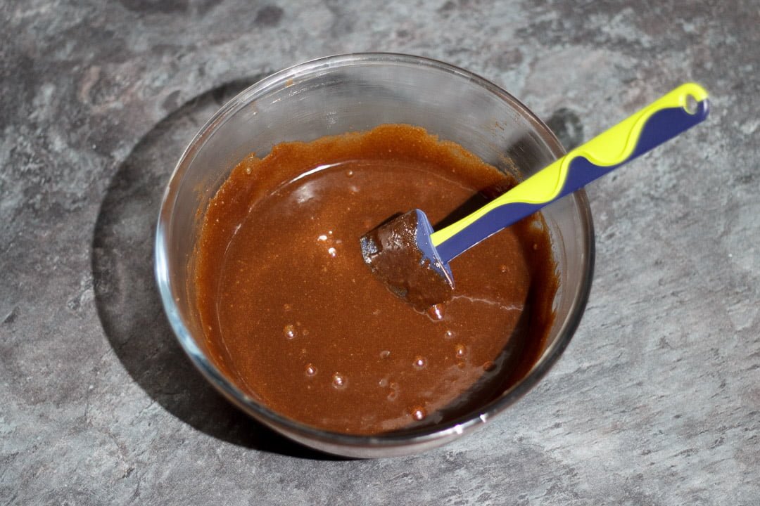 Melted chocolate, butter, eggs and sugar in a glass bowl with a rubber spatula