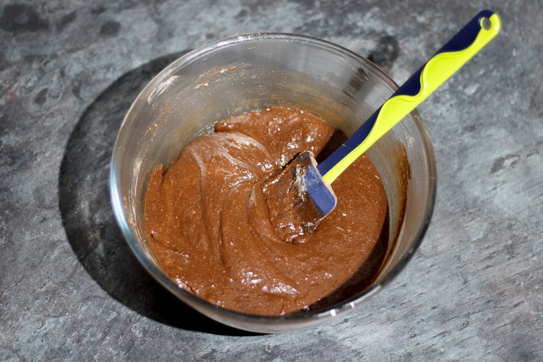 Chocolate brownie batter in a glass bowl with a rubber spatula