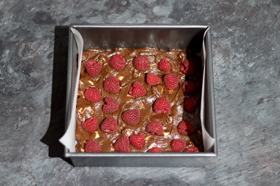 Brownie batter in a lined square baking tin topped with whole raspberries