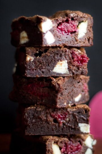 White chocolate raspberry brownies in a stack on a wooden worktop