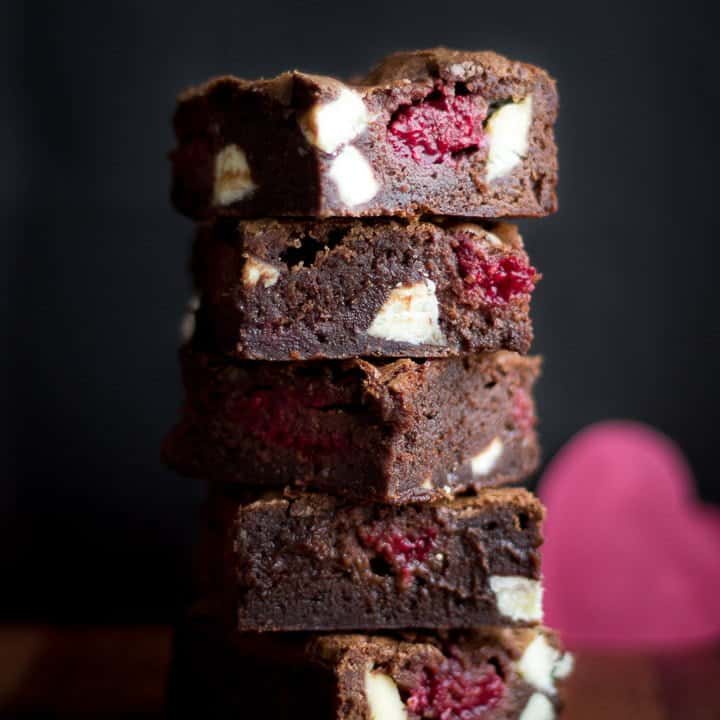 White chocolate raspberry brownies in a stack on a wooden worktop