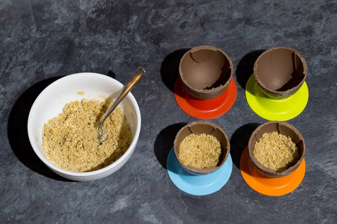 Easter egg bowls being filled with buttery biscuit crumbs