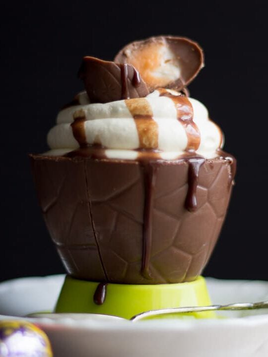 No bake Easter cheesecake in an Easter egg bowl topped with whipped cream, mini Creme Eggs and chocolate sauce.