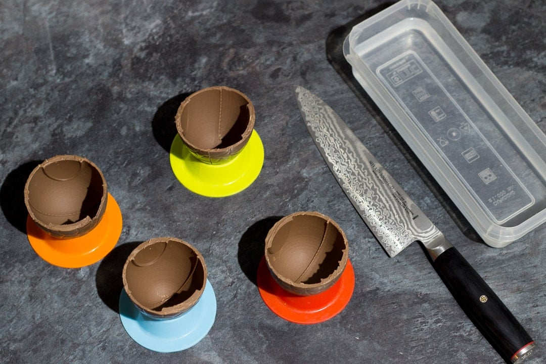 Easter Eggs that have been sliced in half to make bowls, sat in egg cups with a sharp knife and plastic tub filled with hot water next to it.