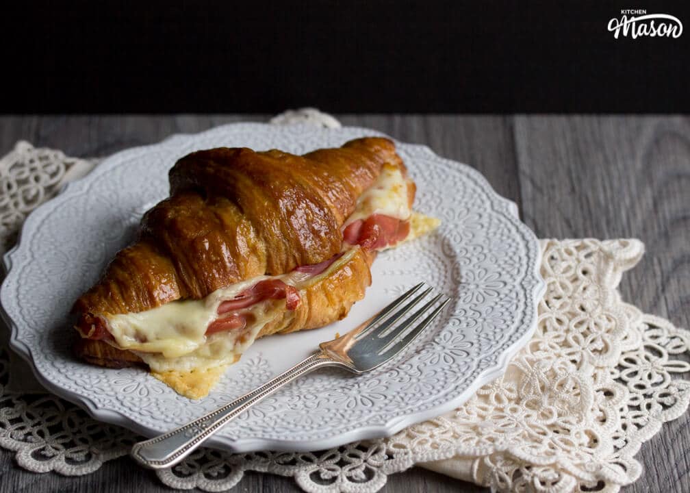 A baked gouda and prosciutto croissant sandwich on a plate with a fork.
