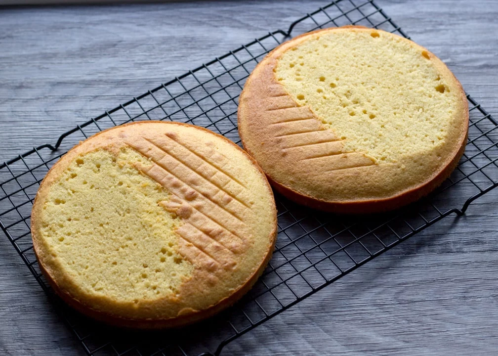 Two sponge cakes on a cooling rack with the domed parts leveled off