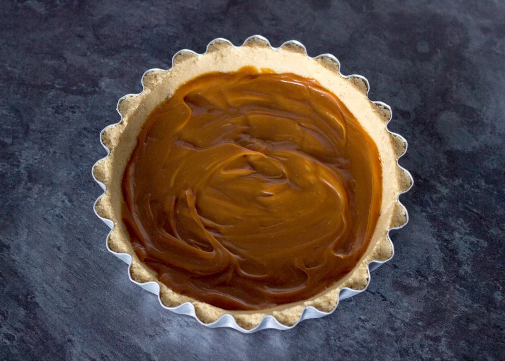 No Bake Caramel Chocolate Tart Recipe: caramel spread out in the bottom of a biscuit base in a fluted tart tin