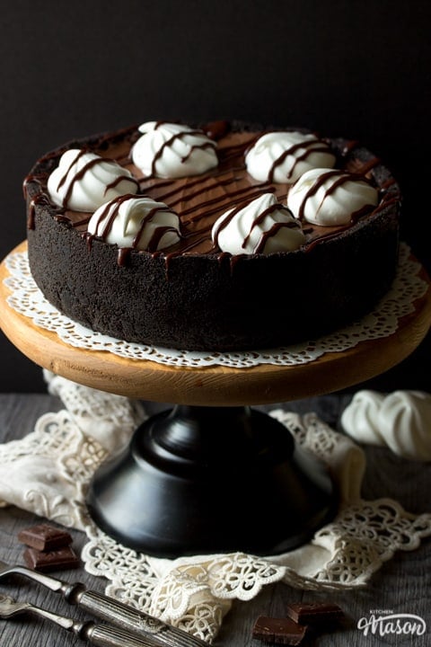 A no bake chocolate cheesecake on a cake stand over a cream napkin