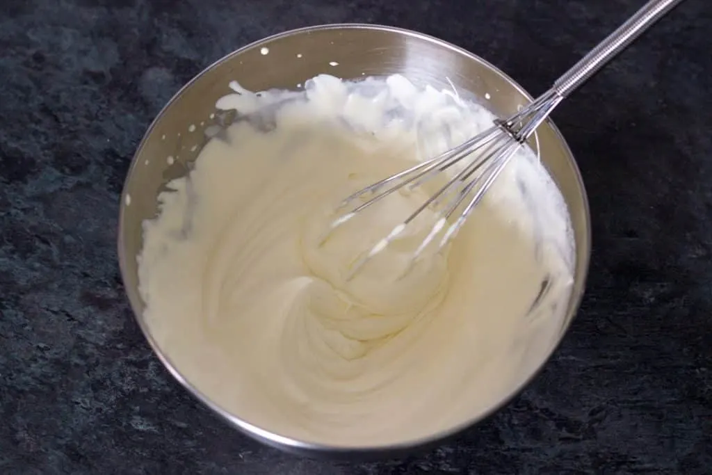 Double cream whipped to soft peaks in a metal bowl with a whisk