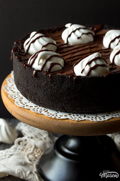 A No Bake Chocolate Cheesecake on a cake stand topped with meringue nests and chocolate sauce