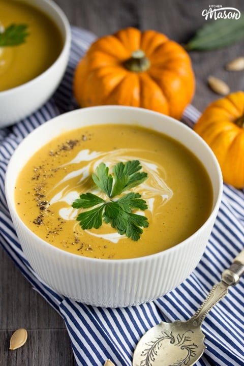 a bowl of slow cooker pumpkin soup with munchkin pumpkins in the background