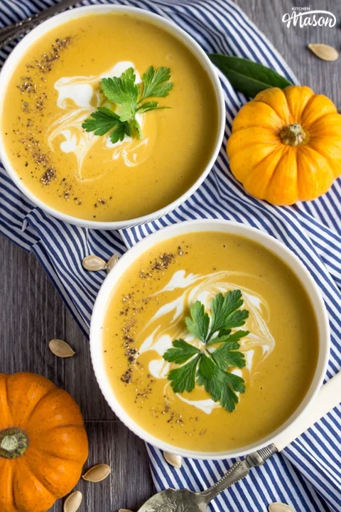 two bowls of slow cooker pumpkin soup topped with cream and parsley