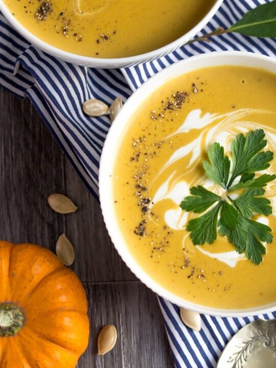 a bowl of slow cooker pumpkin soup with munchkin pumpkins in the background