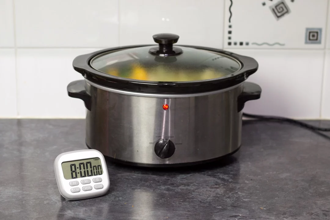 a slow cooker switched on with a timer next to it