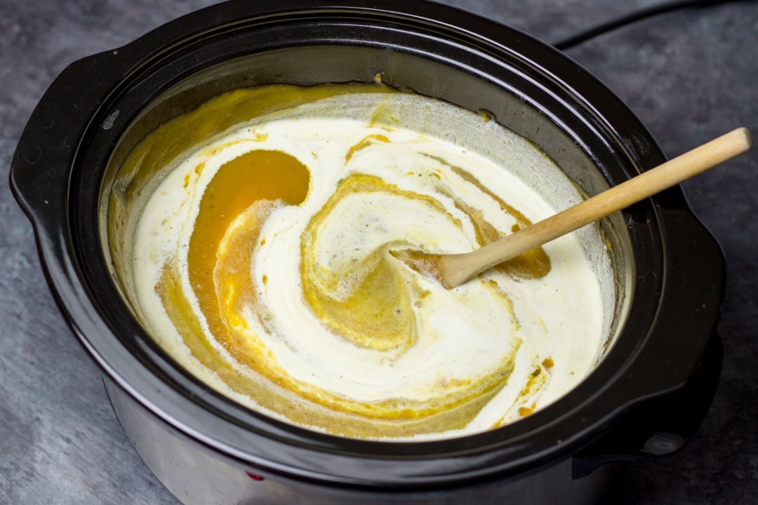 slow cooker pumpkin soup blended in a slow cooker with cream swirled through it