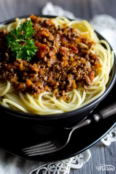Easy spaghetti bolognese in a black bowl with a fork, topped with parsley