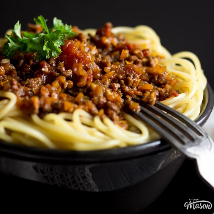 Easy spaghetti bolognese in a black bowl with a fork, topped with parsley