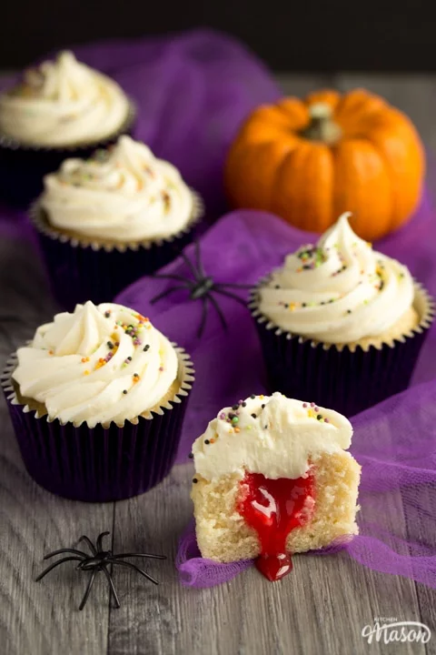 halloween cupcakes cut in half revealing a surprise blood filling with purple tuille and a pumpkin in the background