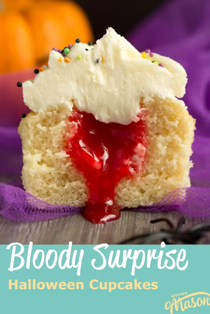 A Halloween cupcake cut in half to reveal a surprise lemon curd 'blood' filling. Set on a grey backdrop with purple netting, black plastic spiders and a small pumpkin in the background. A text overlay says " bloody surprise Halloween cupcakes".