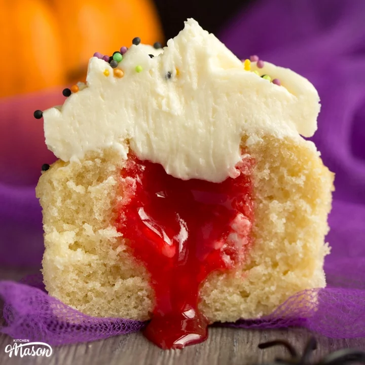 halloween cupcakes cut in half revealing a surprise blood filling with purple tuille and a pumpkin in the background