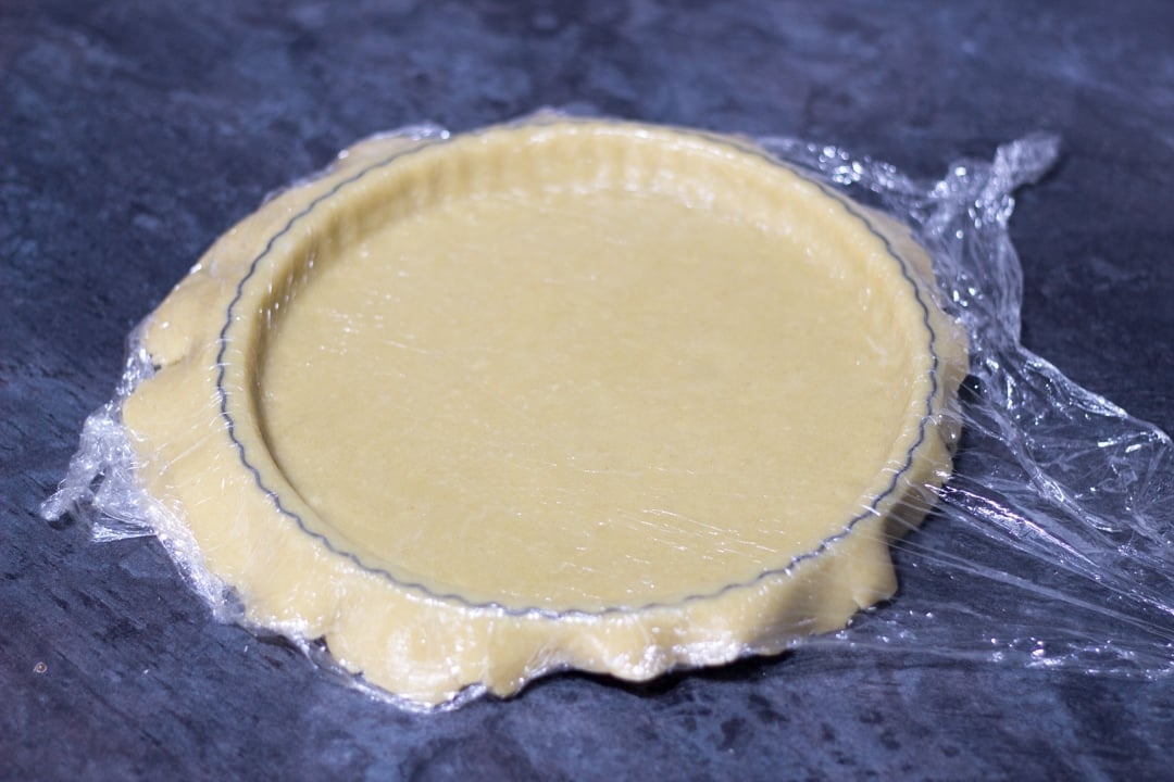 shortcrust pastry lining a tin with the excess hanging over the edge