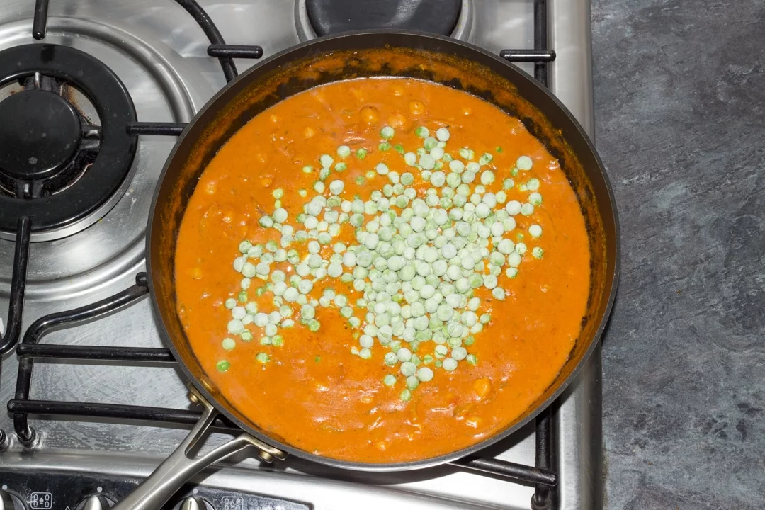 chickpea curry in a saucepan simmering with frozen peas on top