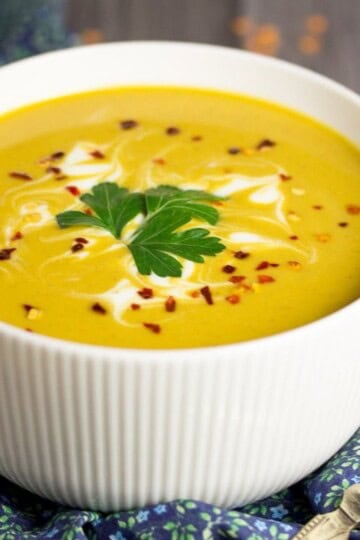 curried coconut lentil soup in a bowl with parsley and chilli flakes on top