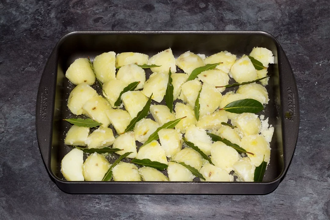 boiled potatoes in a roasting dish drizzled in olive oil and bay leaves