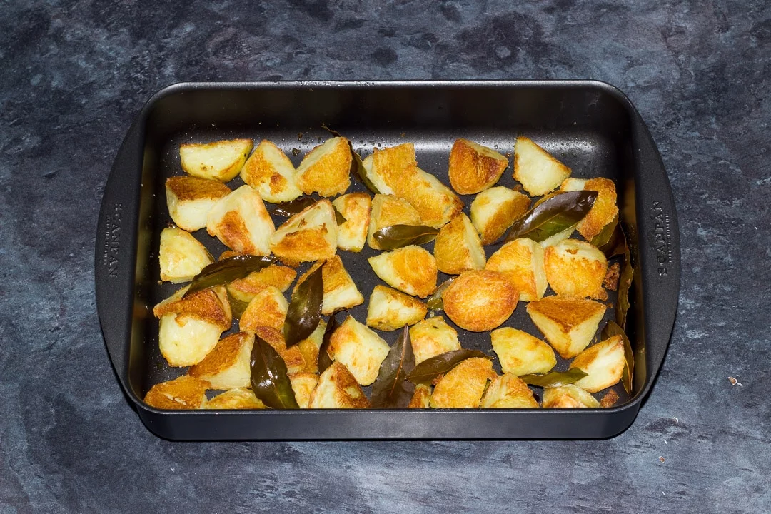 golden crispy roast potatoes in a roasting dish with bay leaves