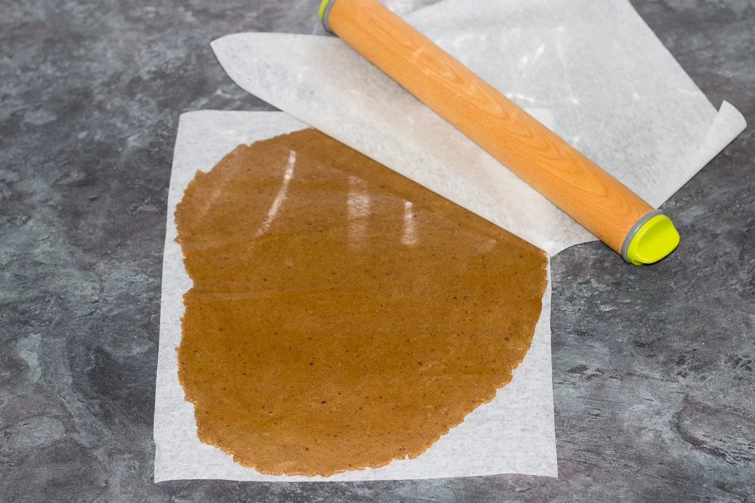 gingerbread dough rolled out between two sheets of baking paper