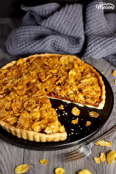 a cornflake tart with a missing slice on a black plate with crumbs around it