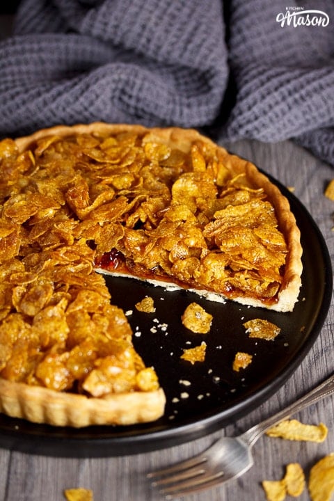 a cornflake tart with a missing slice on a black plate with crumbs around it