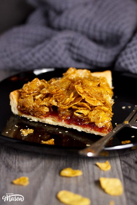 Slice of cornflake tart on a black plate with a fork