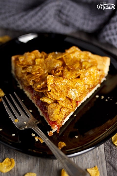 Slice of cornflake tart on a black plate with a fork