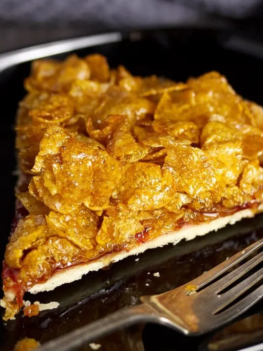 Slice of cornflake tart on a black plate with a fork