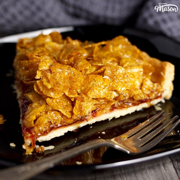 Slice of cornflake tart on a black plate with a fork