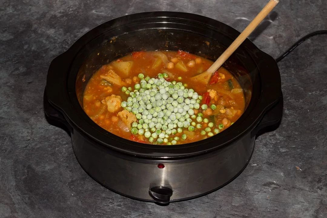 Cooked slow cooker vegetable curry in a slow cooker with frozen peas on top