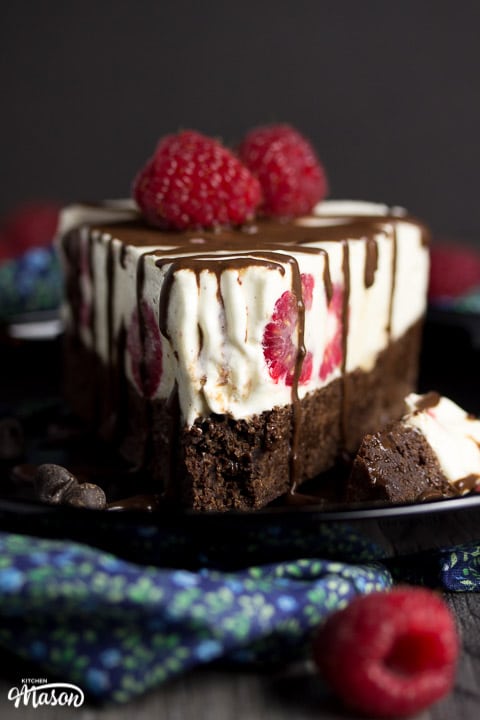 Slice of vegan gluten free raspberry brownie ice cream cake on a black plate drizzle with chocolate sauce and fresh raspberries