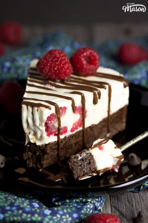 Slice of vegan gluten free raspberry brownie ice cream cake on a black plate drizzle with chocolate sauce and fresh raspberries