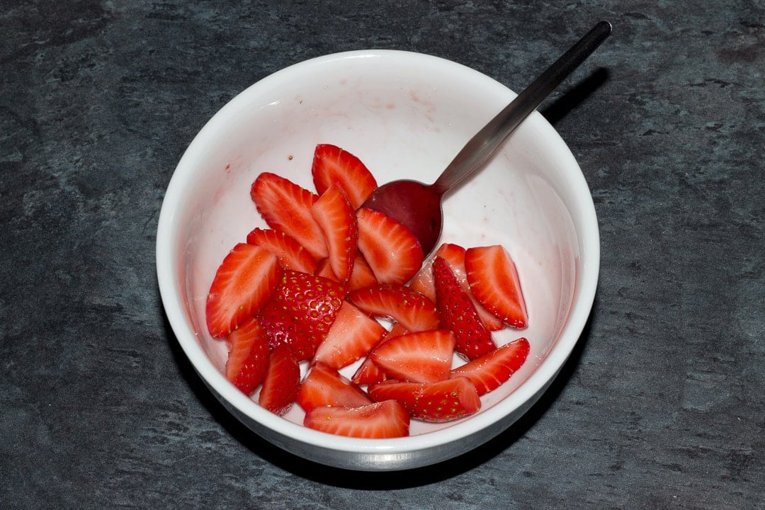 juicy sliced strawberries in a small white bowl with a spoon