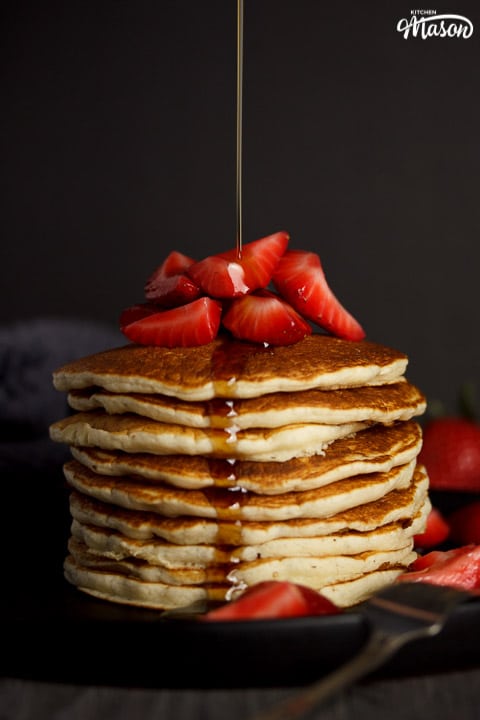 Vegan pancakes in a stack topped with strawberries, drizzled with maple syrup