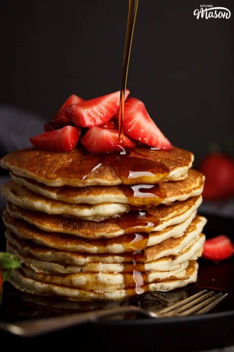 Vegan pancakes in a stack topped with strawberries, drizzled with maple syrup