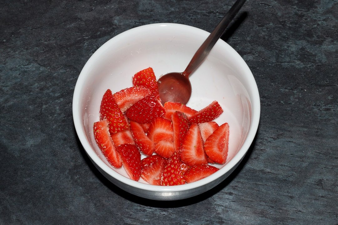 strawberries and sugar in a small white bowl with a spoon