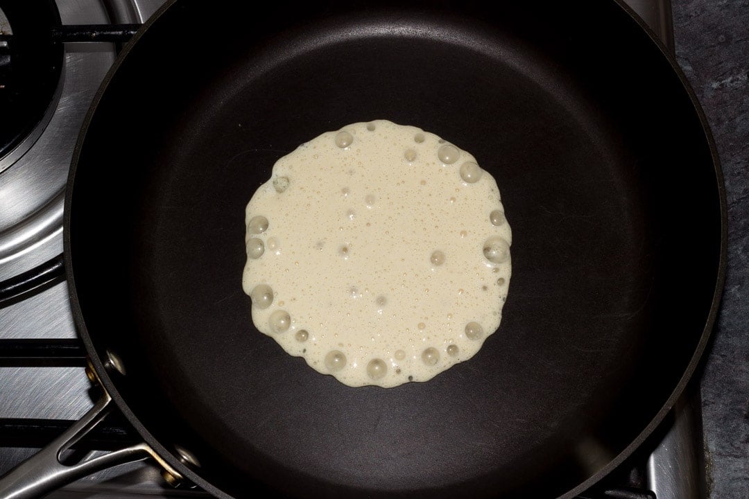 vegan pancake batter bubbling in a frying pan