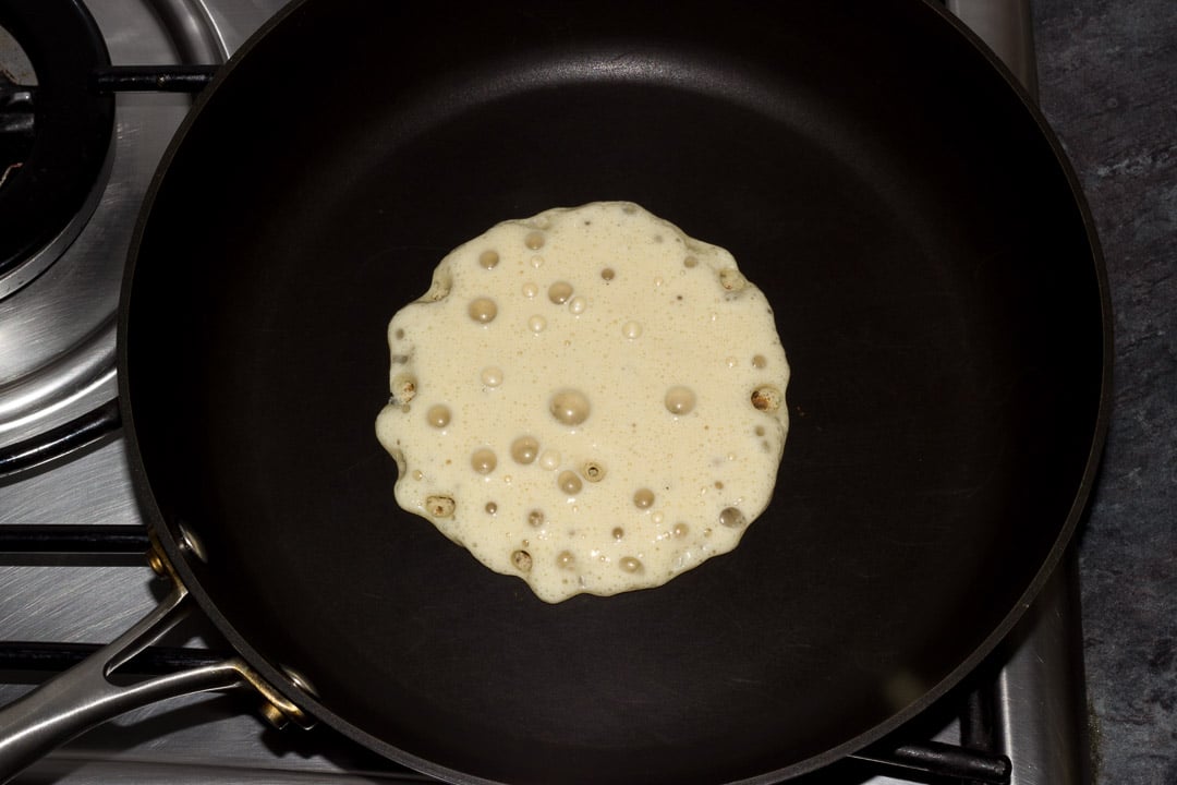 vegan pancake batter bubbling in a frying pan