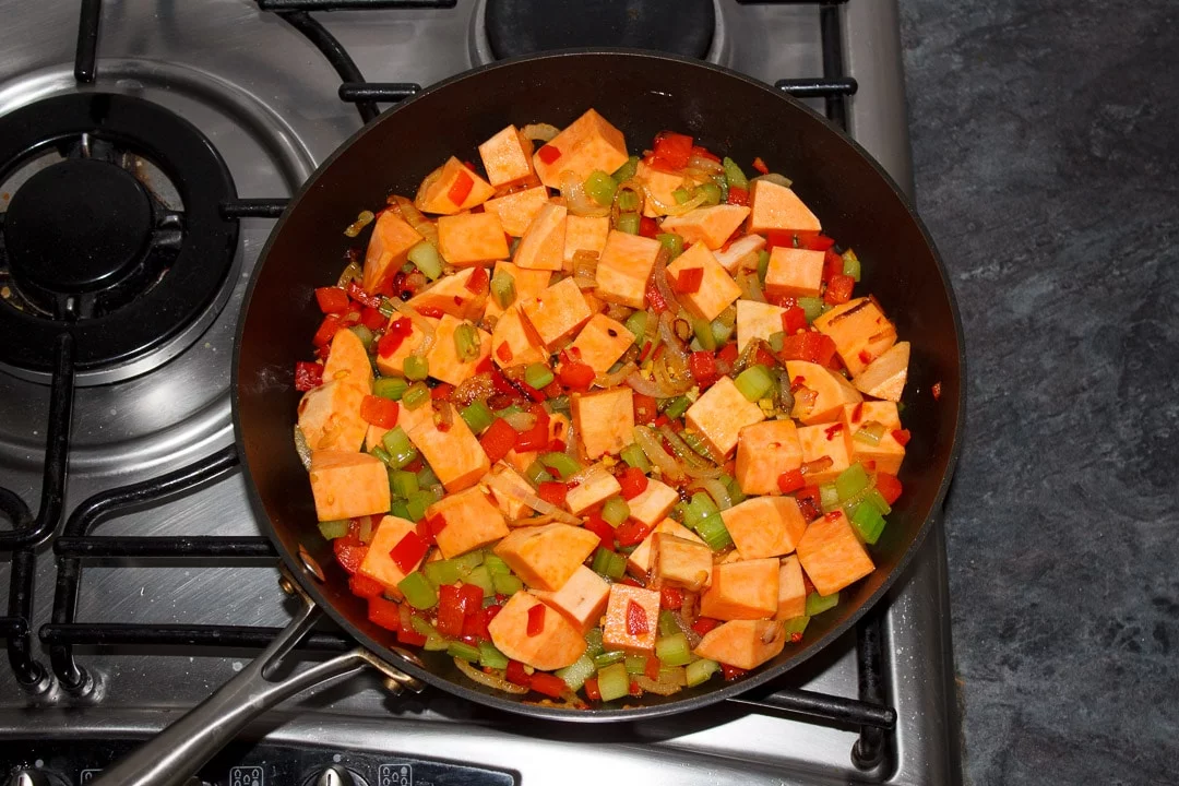 Sweet potato, onion, red pepper, celery, ginger and chilli frying in a frying pan