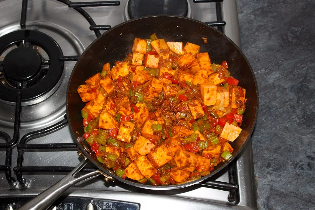 Sweet potato and other vegetables frying in a frying pan covered in curry paste