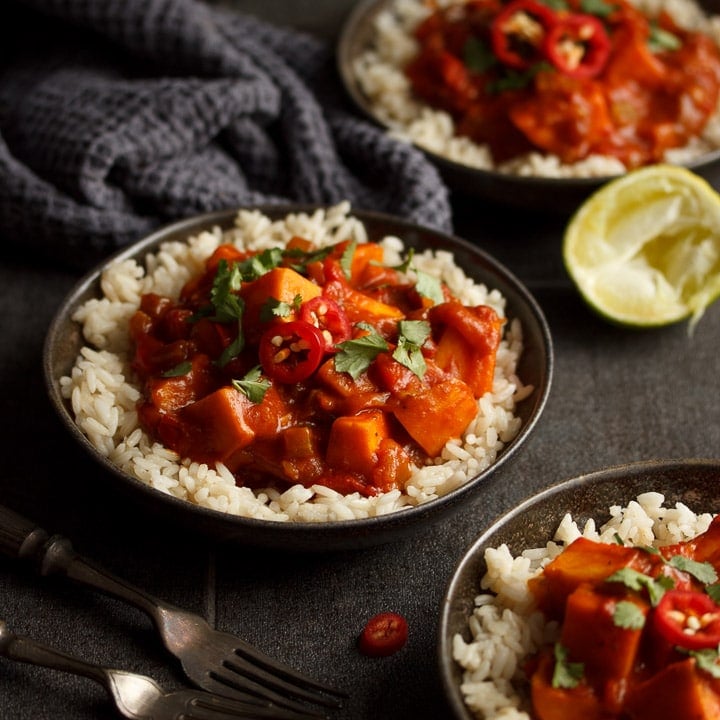 3 bowls of sweet potato curry and rice with fresh limes, forks and a dark grey tea towel