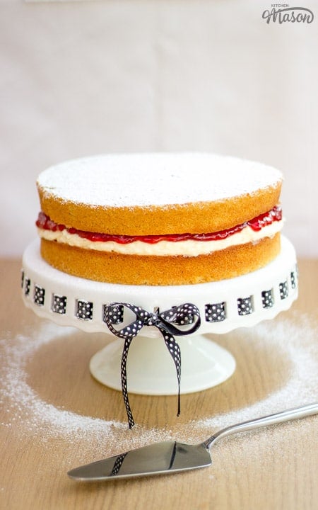 A victoria sandwich cake on a cake stand, dusted with icing sugar.