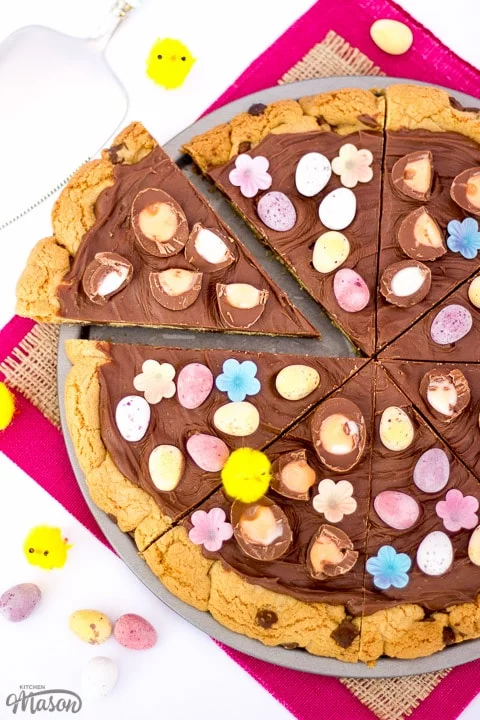 Easter Chocolate Cookie Pizza sliced up on pink fabric with little yellow chicks